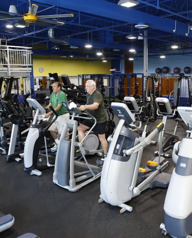 Two adult men use elliptical machines for a cardio workout in an Atlantic Highlands gym cardio floor
