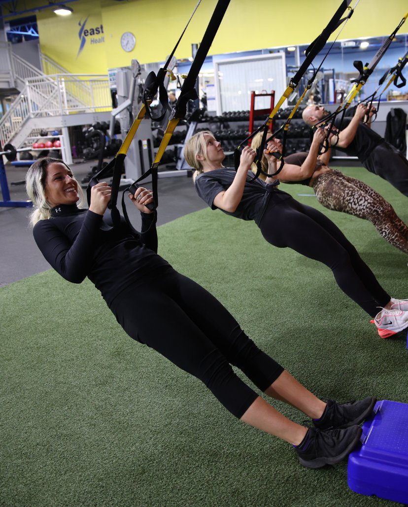 A small group of gym members use tension bands to hold themselves up from a leaning position during a small group training session in the turf area at an Atlantic Highlands gym