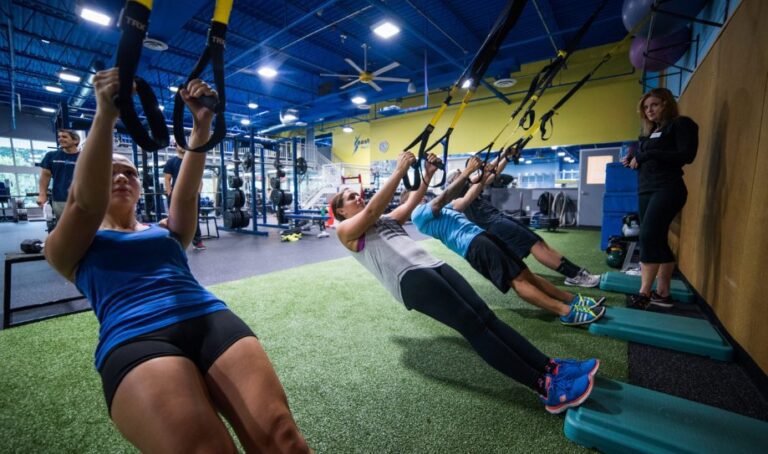 A small group of gym members use tension bands to hold themselves up from a leaning position during a small group training session in the turf area at an Atlantic Highlands gym